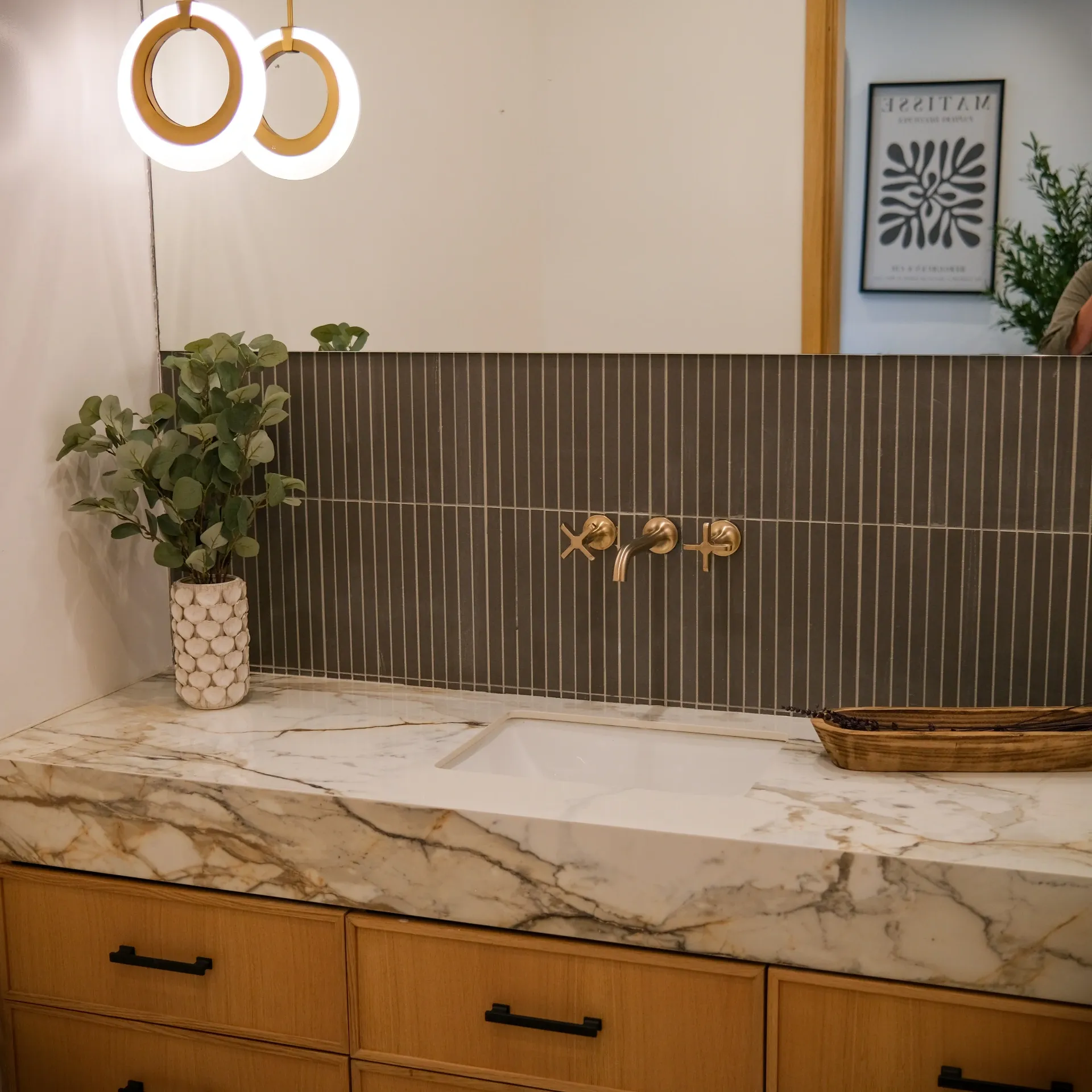 15602 Morrison St — Bathrooms: 15602 Morrison St — Bathroom vanity with marble waterfall countertop, fluted tile backsplash, brass wall-mounted faucets, and modern pendant lighting