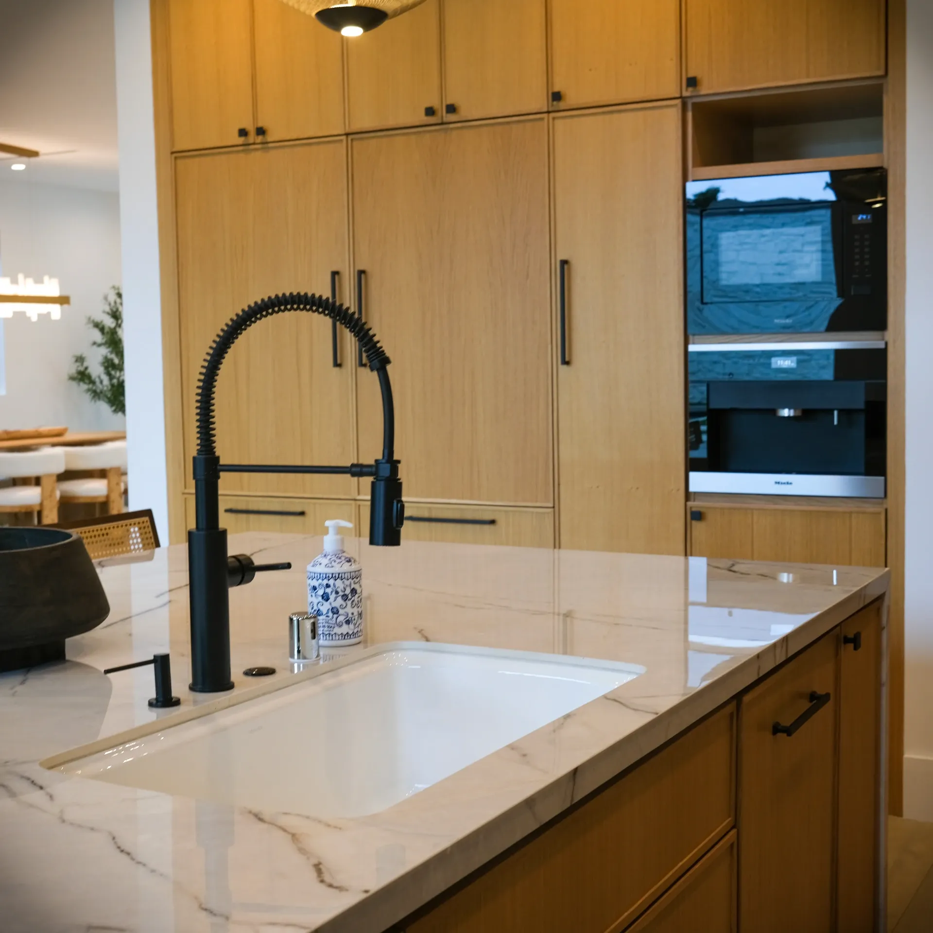15602 Morrison St — Kitchen: 15602 Morrison St — Kitchen island with white marble countertops, wood cabinetry, black fixtures, and integrated appliances