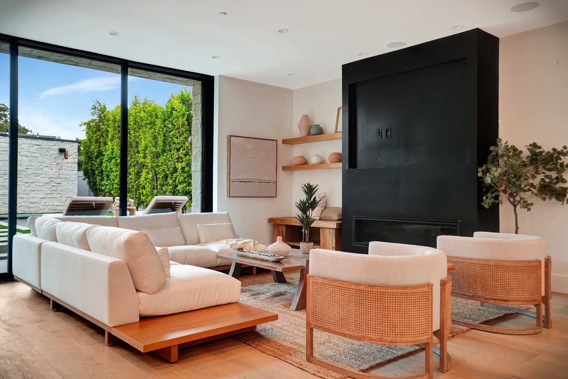 15602 Morrison St — Living Areas: 15602 Morrison St — Living room with white sectional sofa, cane accent chairs, black fireplace, and garden courtyard views